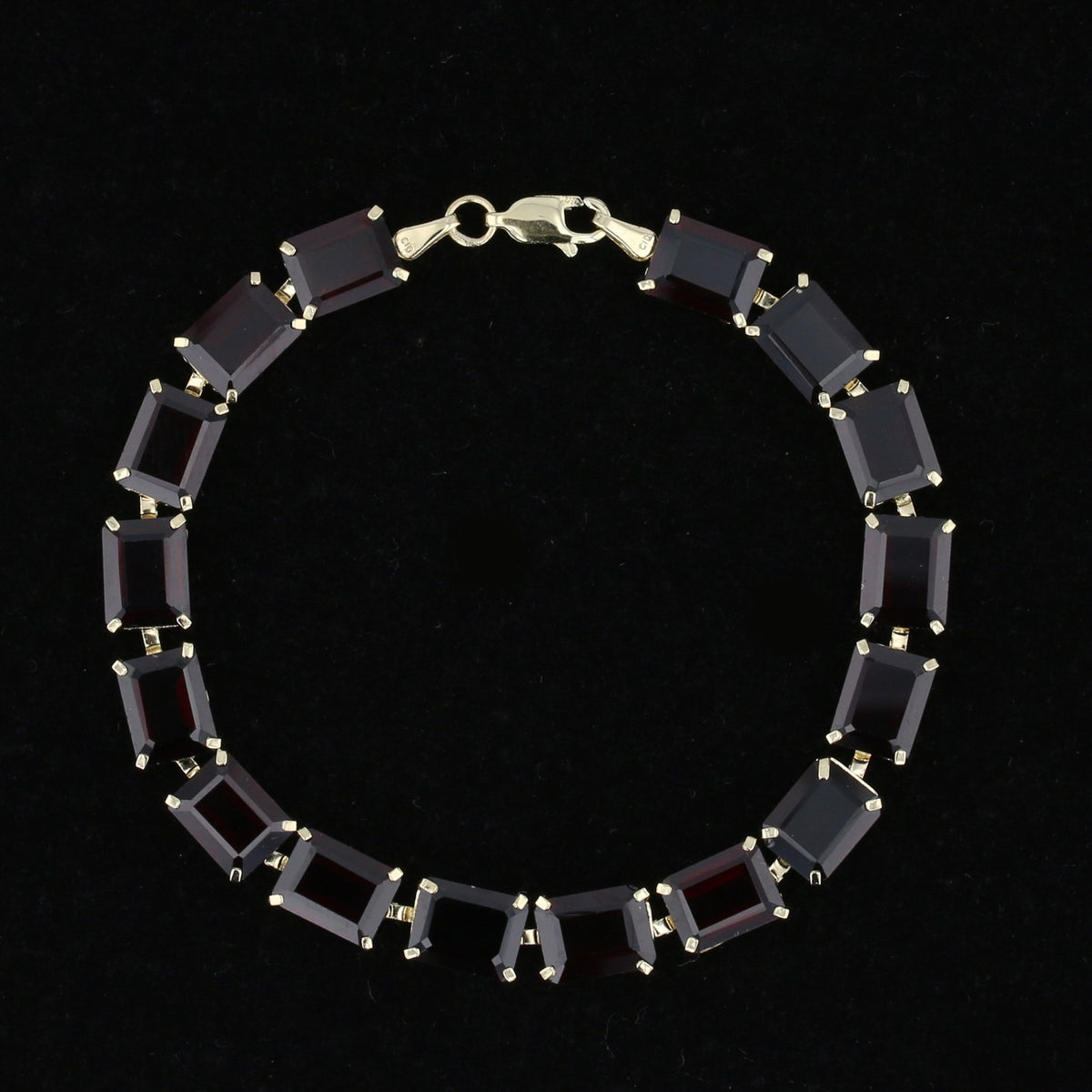 Vintage 10K gold line bracelet with emerald-cut red garnets, laid flat. Item 894562.