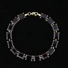 Vintage 10K gold line bracelet with emerald-cut red garnets, laid flat. Item 894562.