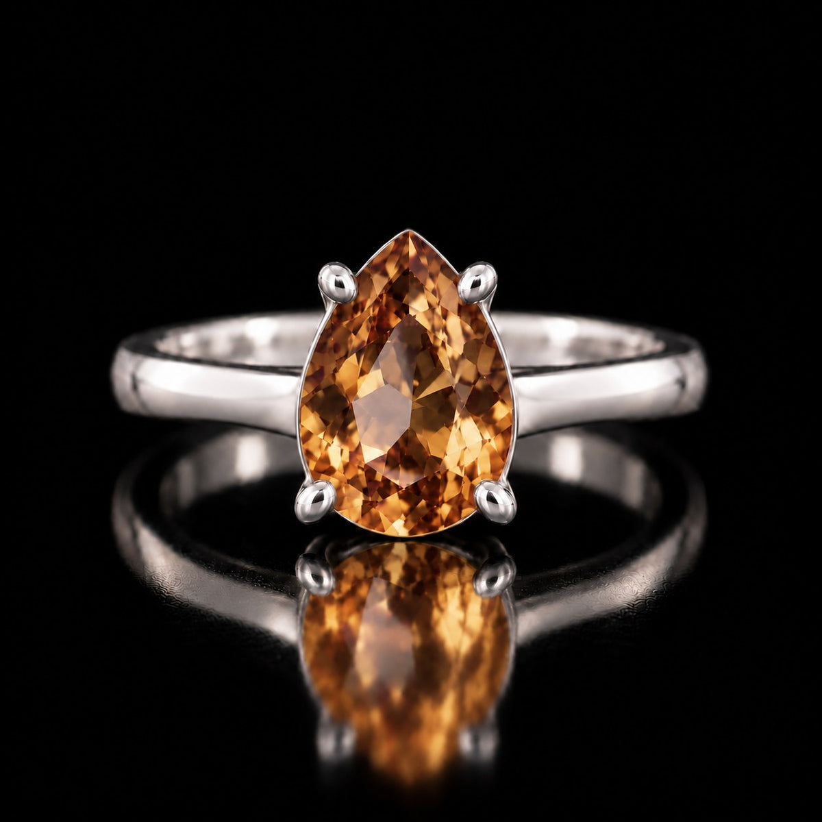 The same VooDooStone pear-cut solitaire ring turning golden amber under warm incandescent light, front view. Item 894782.