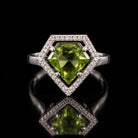 The same VooDooStone shield-cut halo ring turning peridot green under fluorescent light, front view. Item 894784.